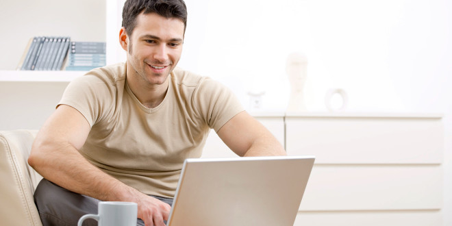 Happy young man in t-shirt sitting on sofa at home, working on laptop computer, smiling.; Shutterstock ID 29143153; PO: The Huffington Post; Job: The Huffington Post; Client: The Huffington Post; Other: The Huffington Post